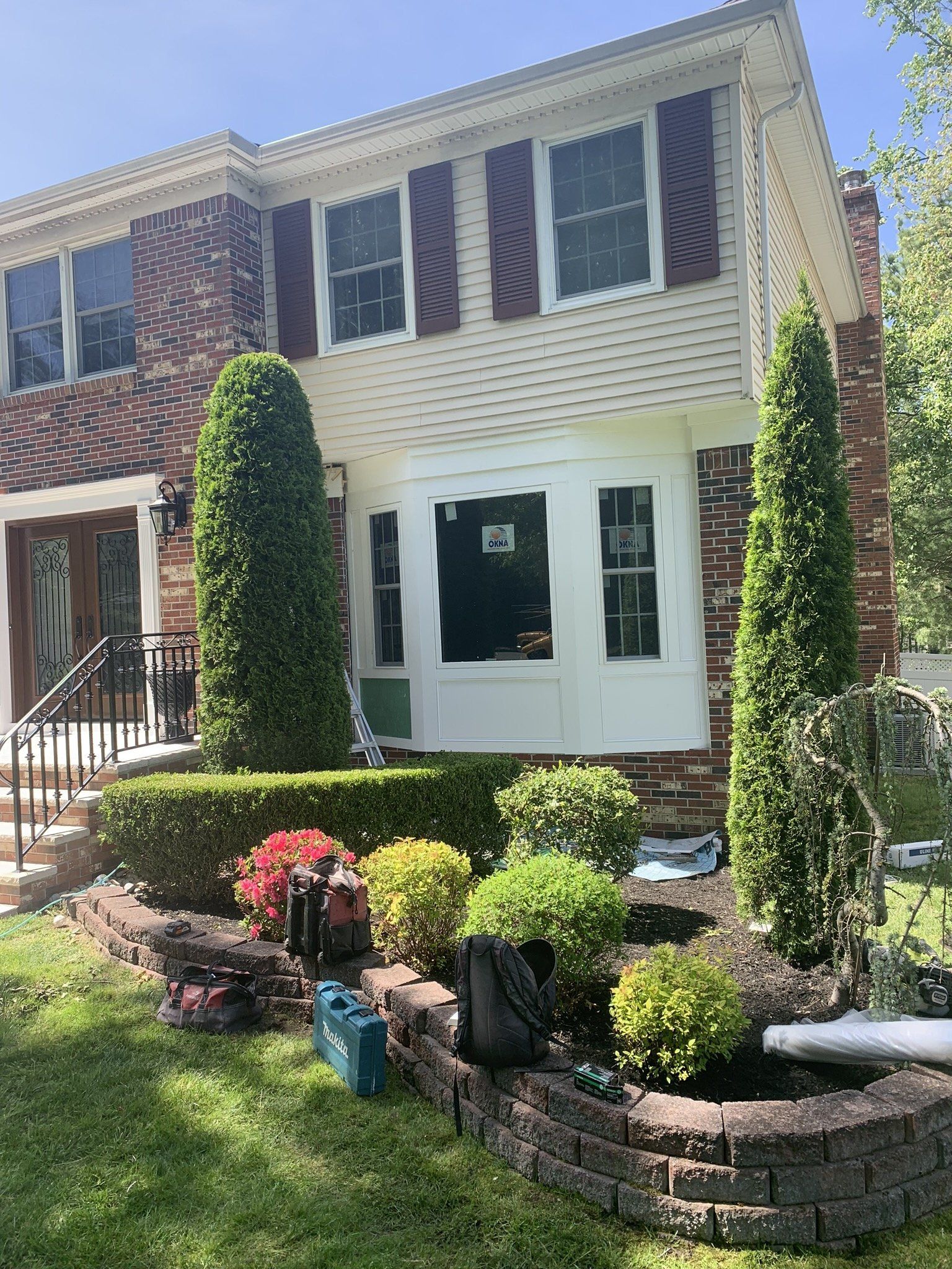 Two-story brick townhouse with white sunroom, striped shutters, and landscaped front garden