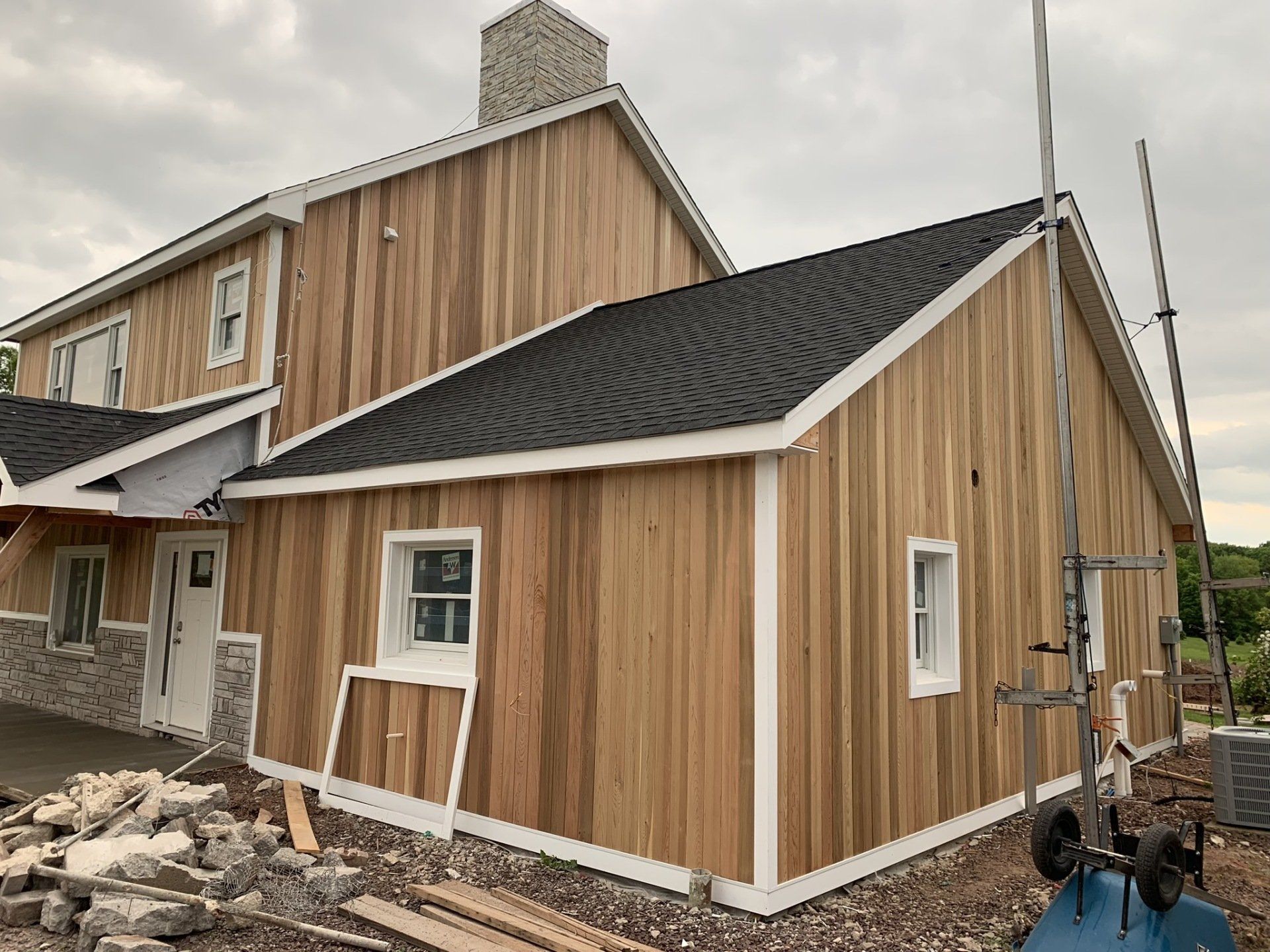 New house exterior with vertical wood siding, black roof, and unfinished landscaping debris around it