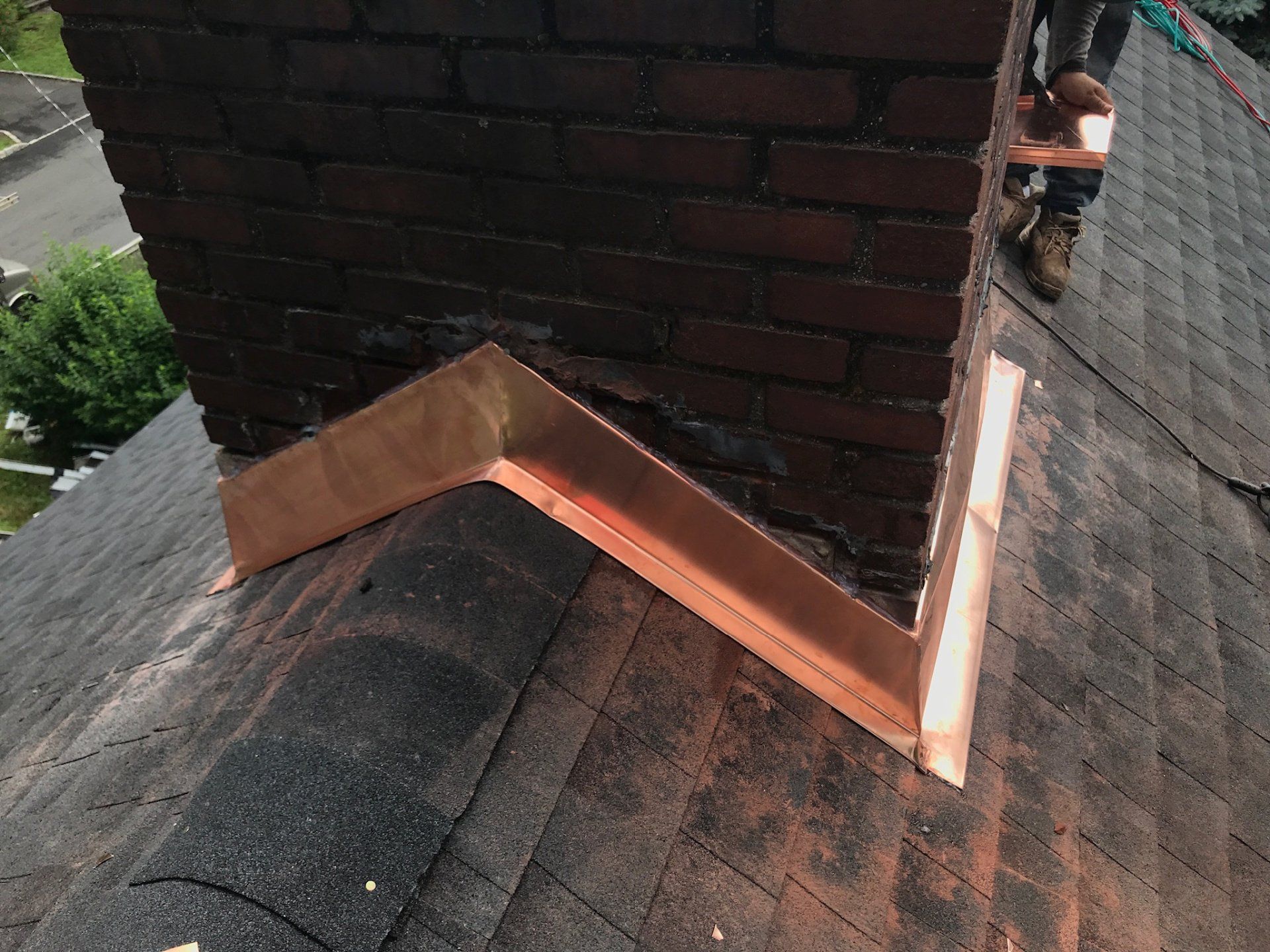 Damaged roof valley with exposed copper flashing around a brick chimney.