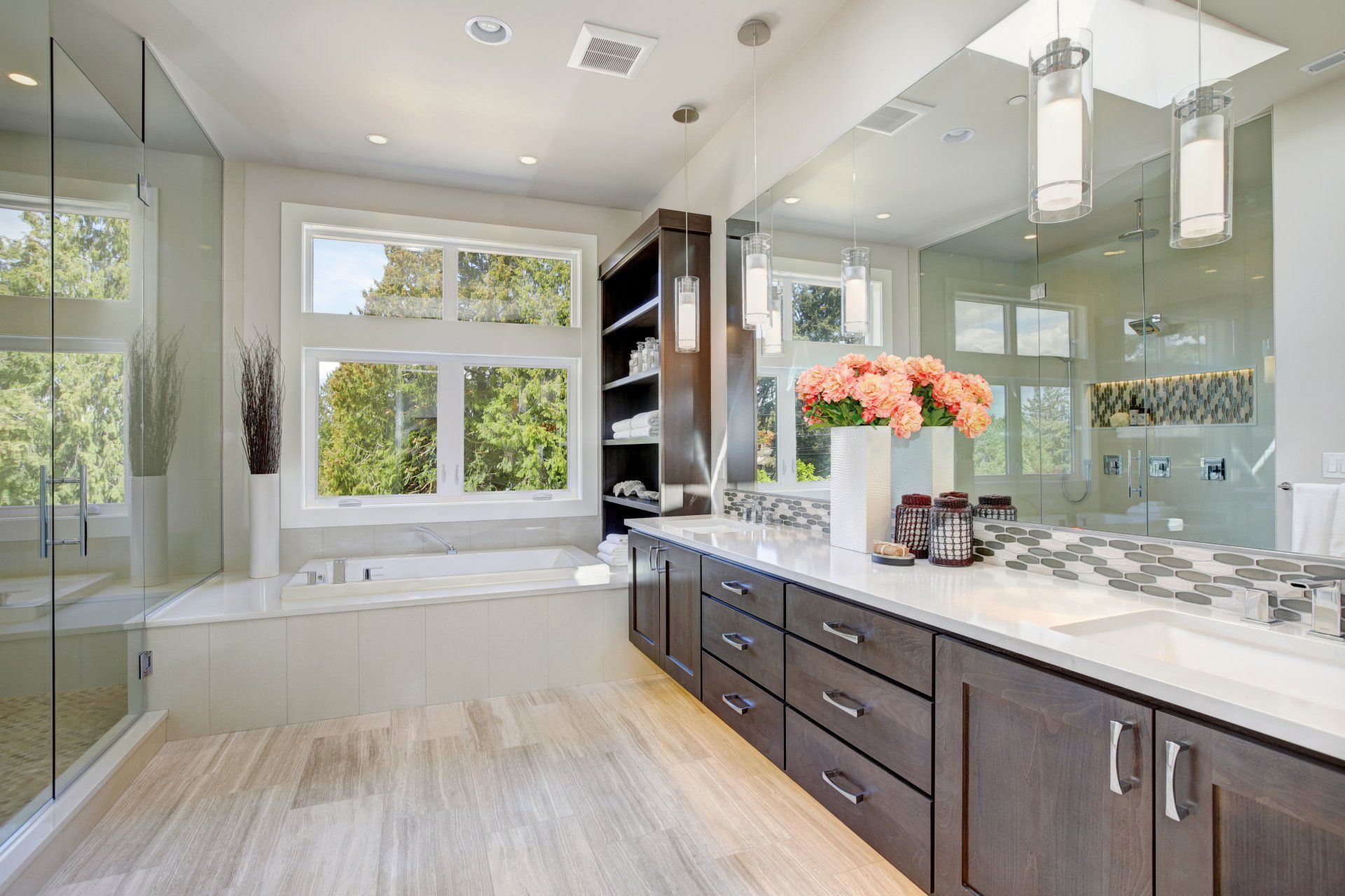 Modern bathroom with freestanding tub, double vanity, glass shower, and large windows overlooking greenery