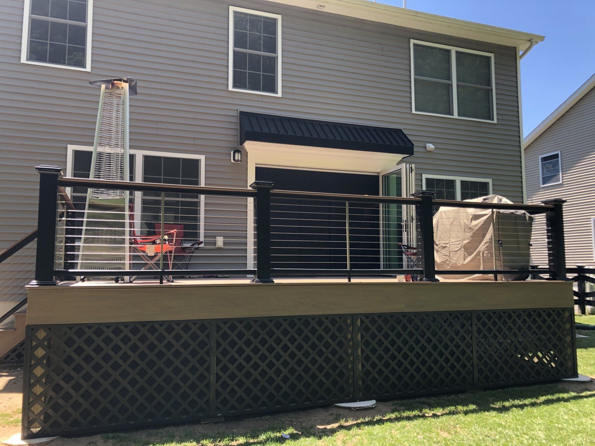 Backyard deck with black railing, lattice skirt, patio furniture, and sliding doors on a house