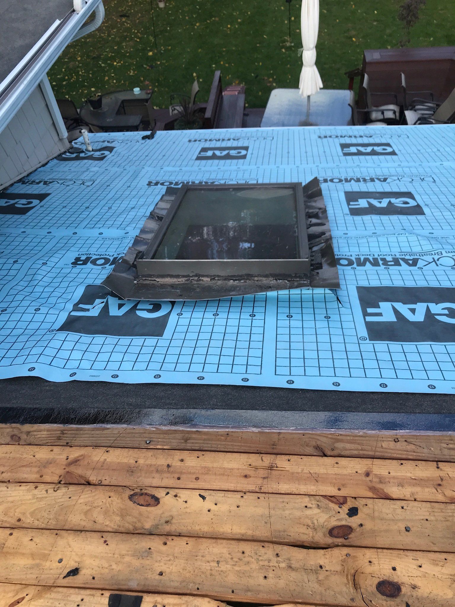 Blue roofing underlayment around a skylight on a sloped roof, with wood framing at the bottom.