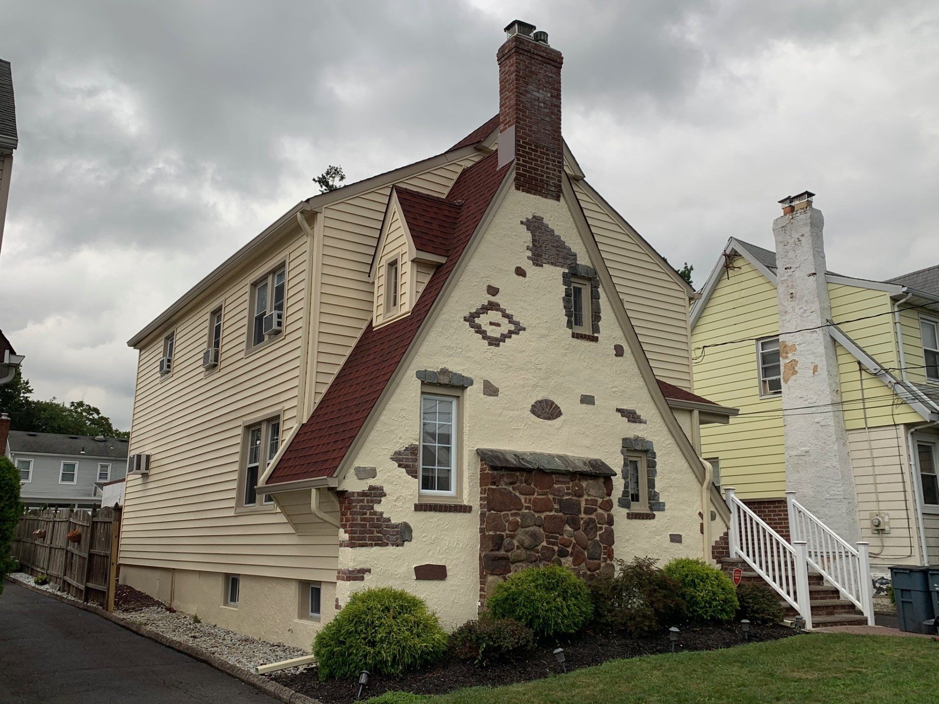Deteriorating two-story house with peeling cream siding and red trim under a cloudy sky