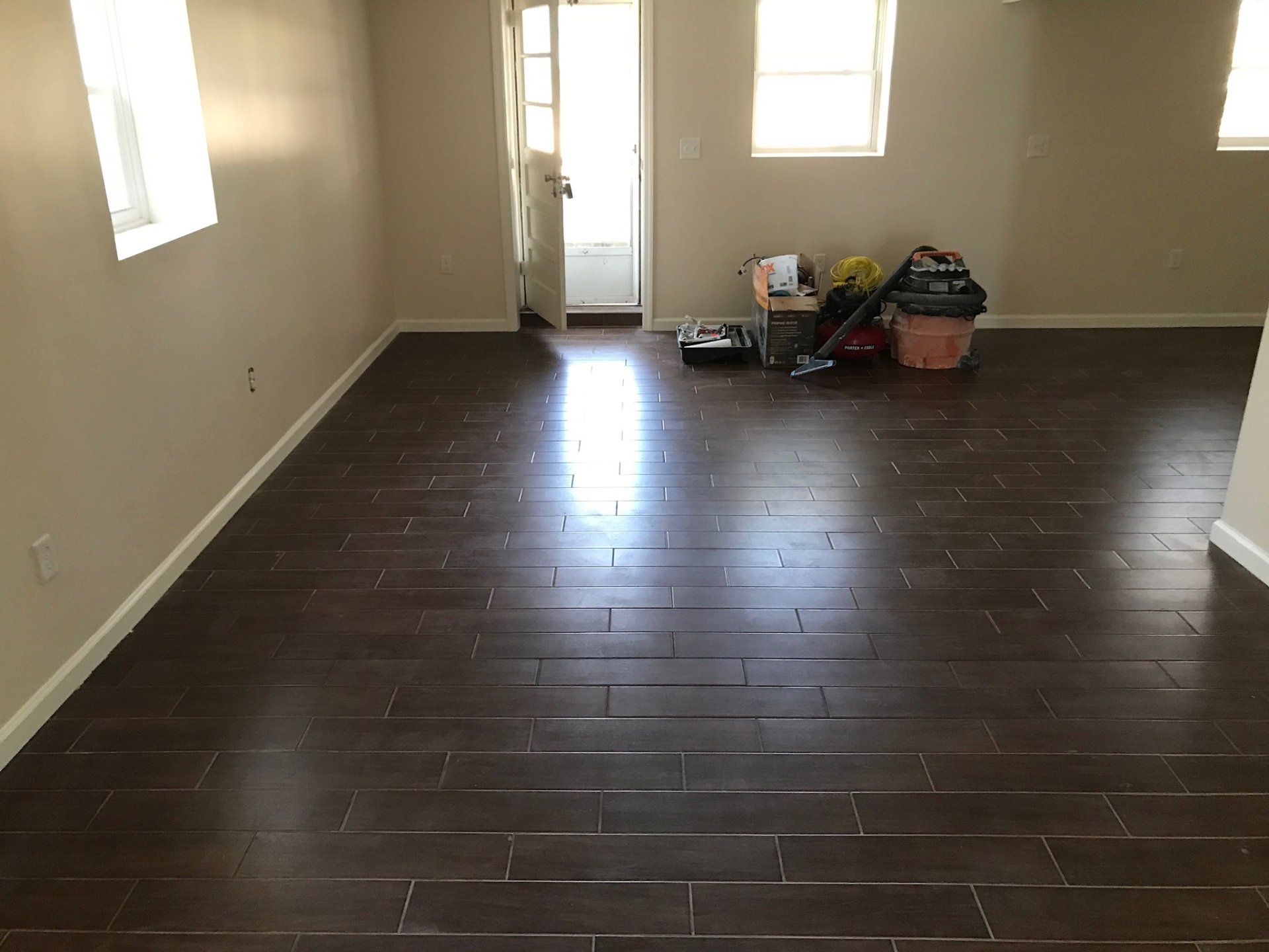 Empty living room with dark wood floors, beige walls, and belongings stacked near the back door