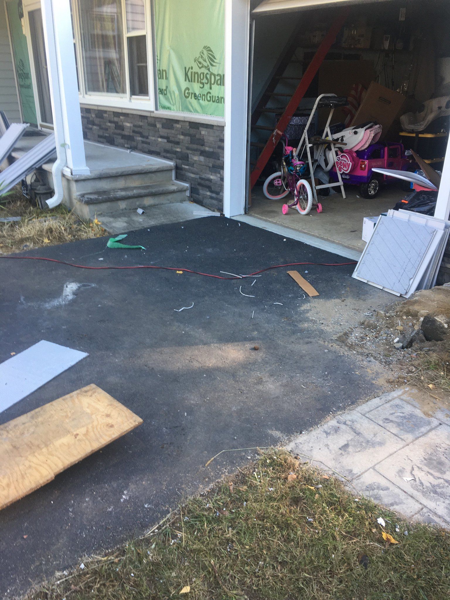 Damaged driveway leading to a garage, with debris, broken boards, and a child’s bike inside.