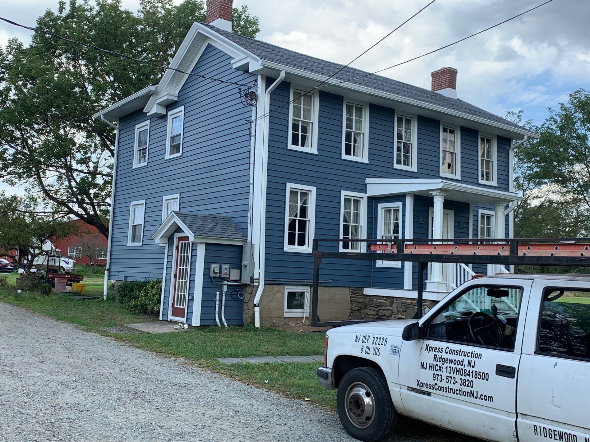 Blue two-story house with white trim and a white work truck parked in front on a gravel lot