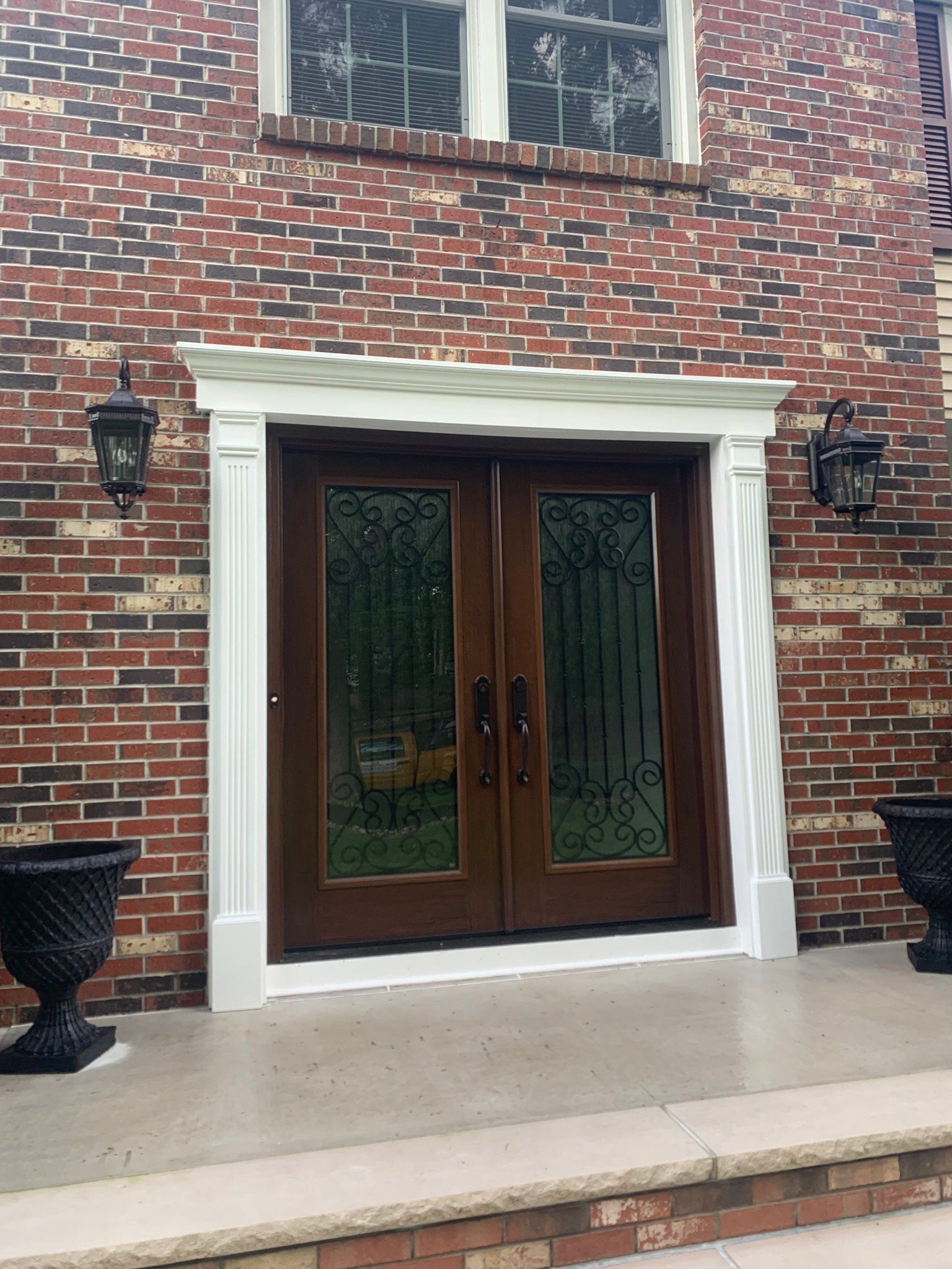 Brick house entrance with dark wooden double doors, white trim, and wall lanterns.