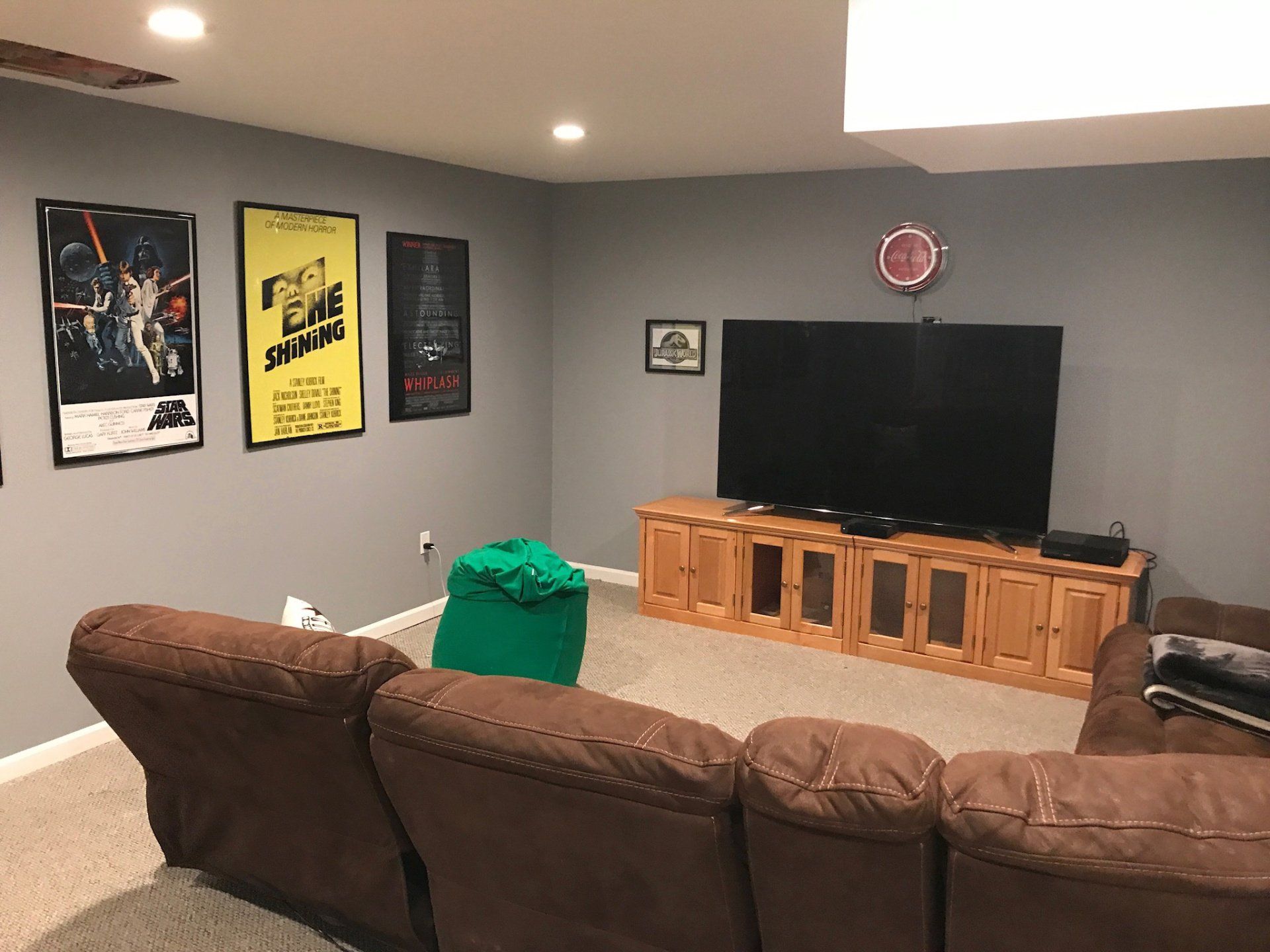 Basement TV room with brown sectional, wall posters, large flat-screen, and wooden media console