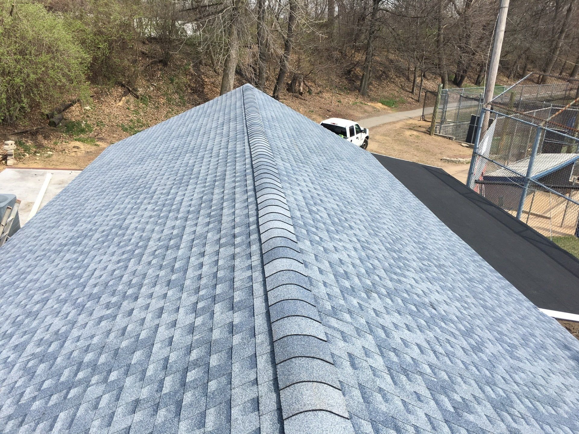 Aerial view of a gray shingled roof with trees and a driveway in the background