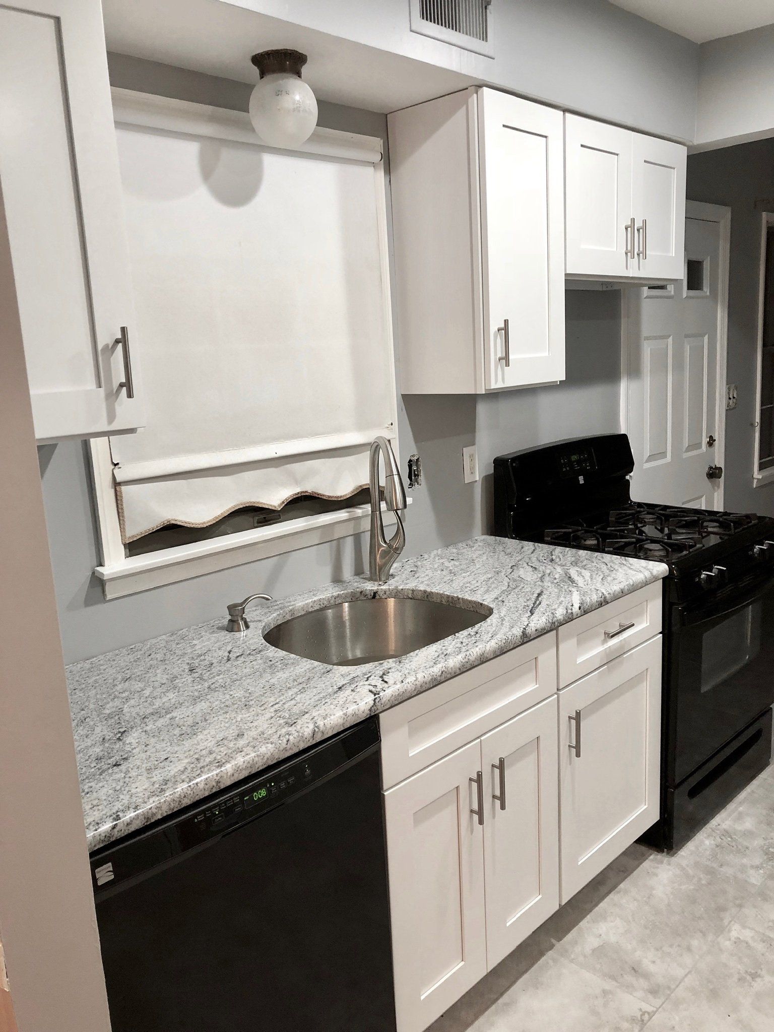 Compact white kitchen with granite counters, sink, black stove, and upper cabinets