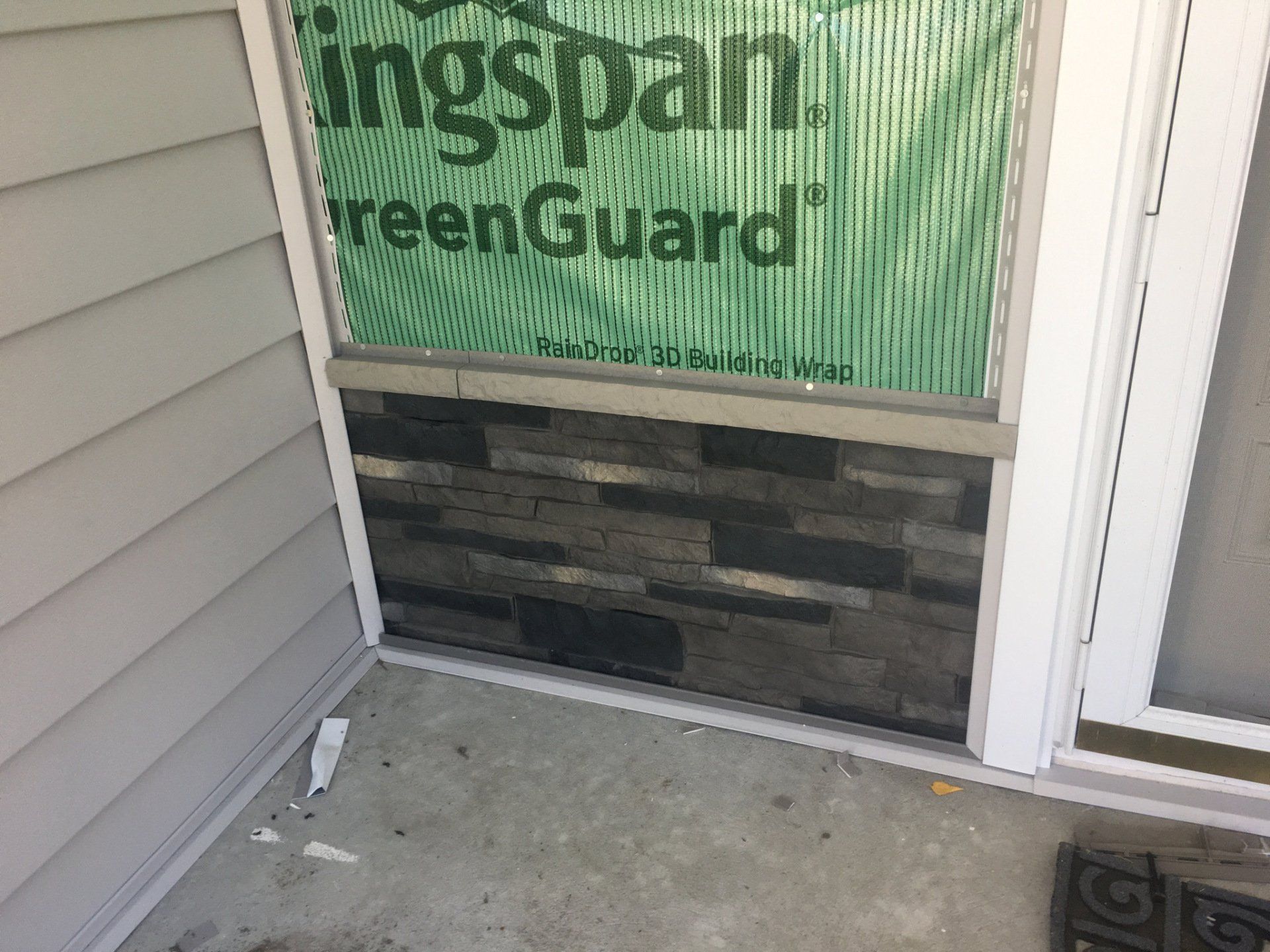 Front entry with unfinished concrete porch, stone veneer below a screened window, and white siding door frame