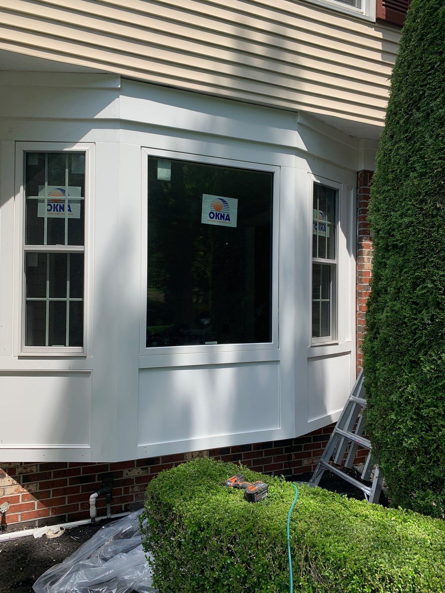 House exterior with white bay window, brick base, and landscaped hedge in front