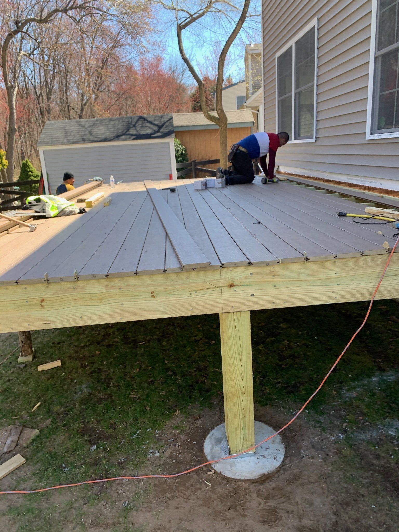 Partially built gray deck attached to a house, with two workers installing boards outdoors