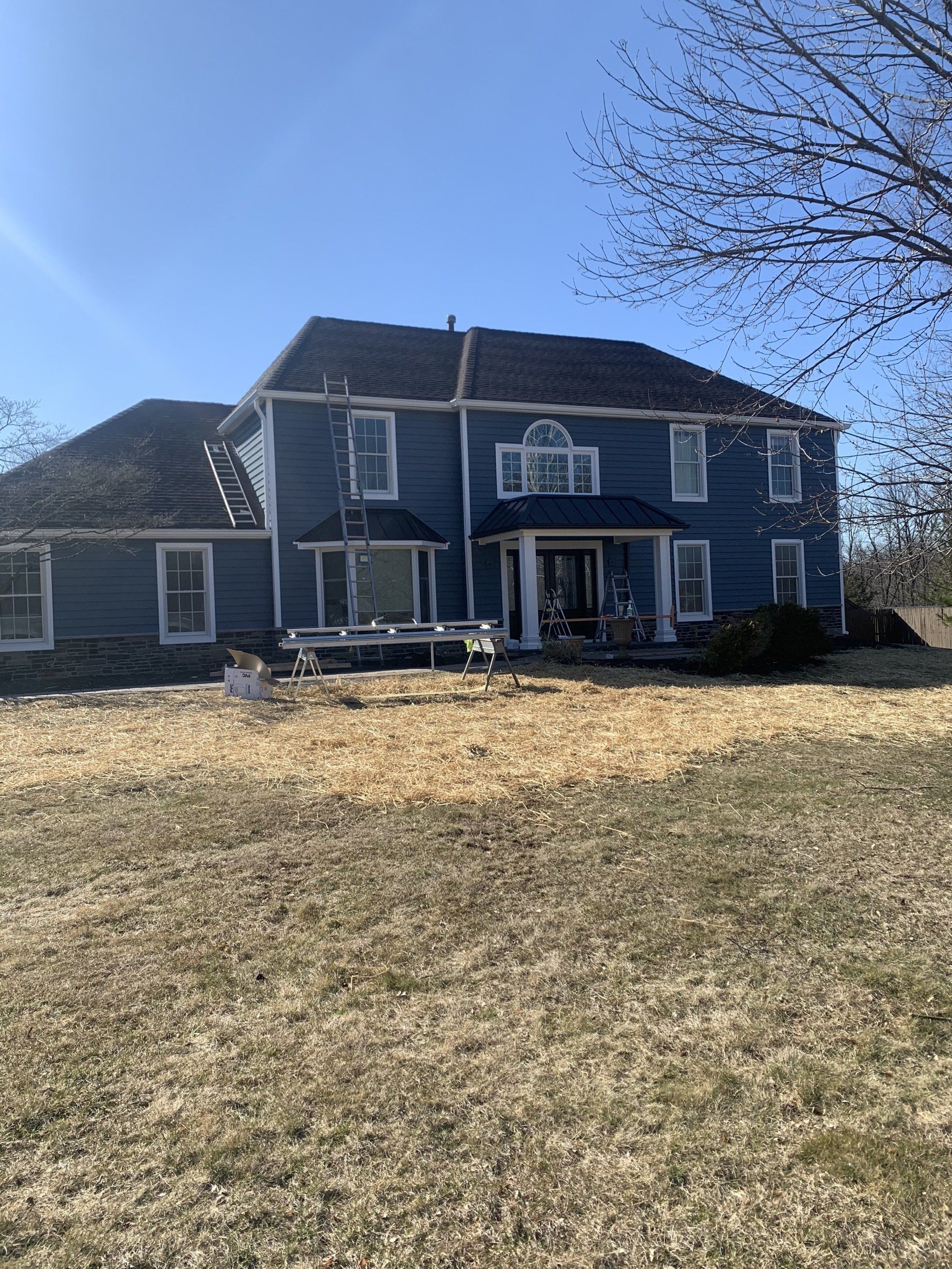 Large blue two-story house with white trim on a grassy slope under a clear sky