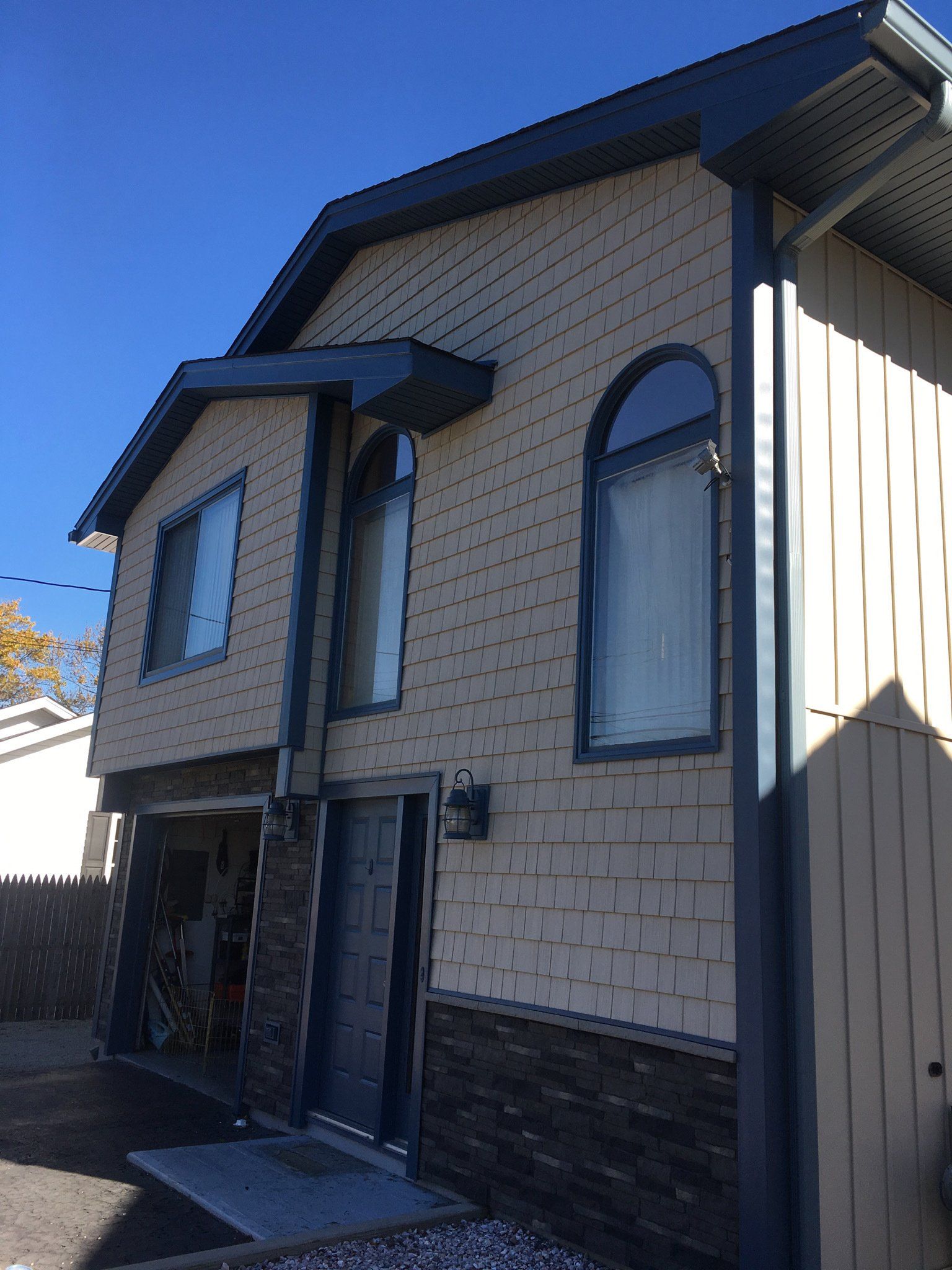 Two-story beige house with blue trim and arched windows, viewed from the side on a sunny day.