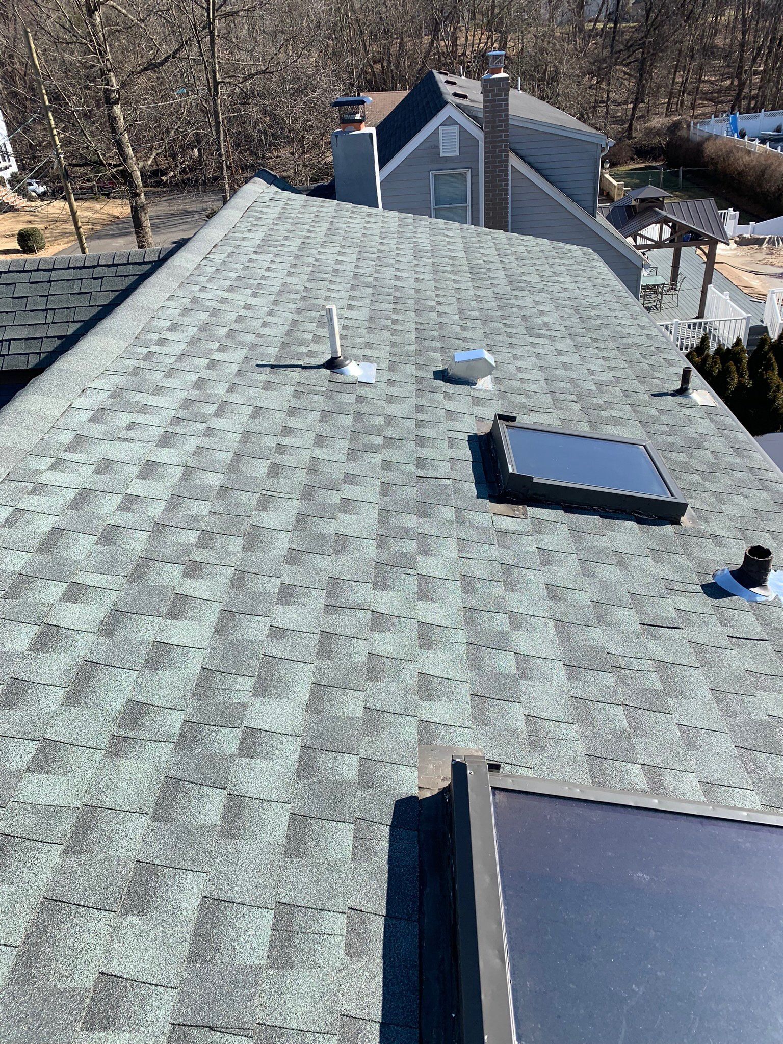 Rooftop with gray shingles, vents, and skylights under bright daylight