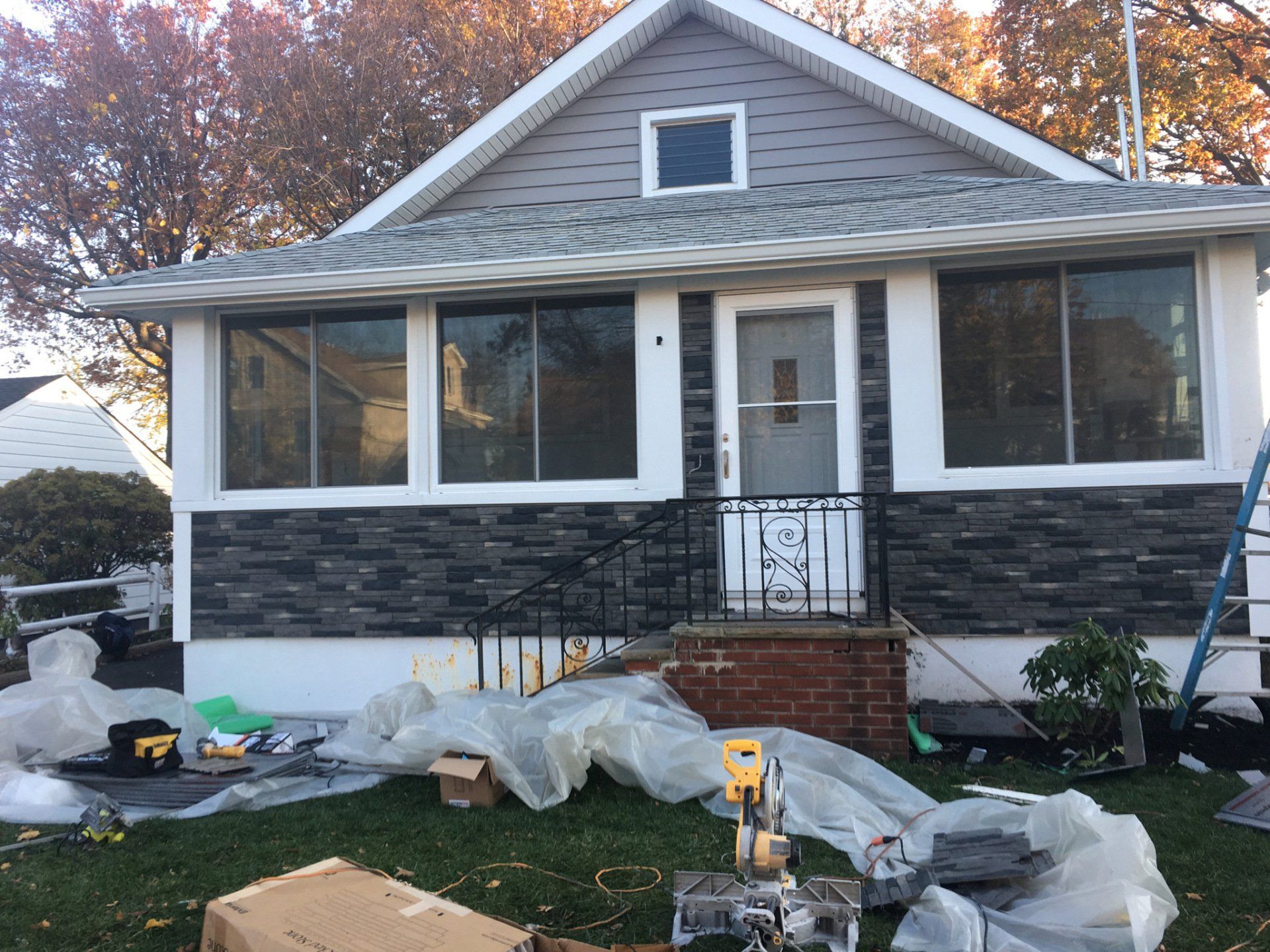 House front porch under renovation with plastic sheeting, debris, and ladder on the lawn