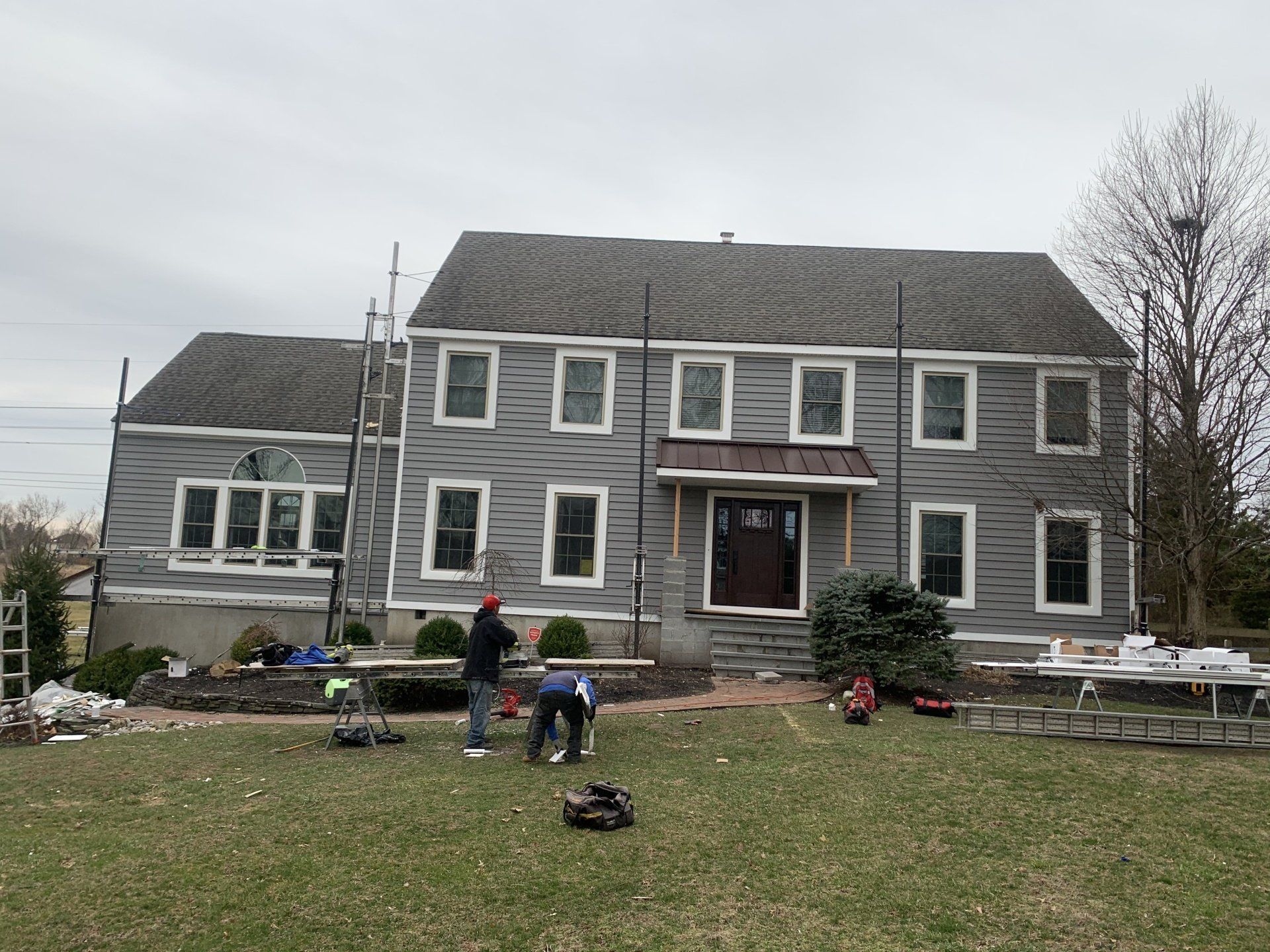 Gray house under renovation with workers in the front yard and ladders against the siding