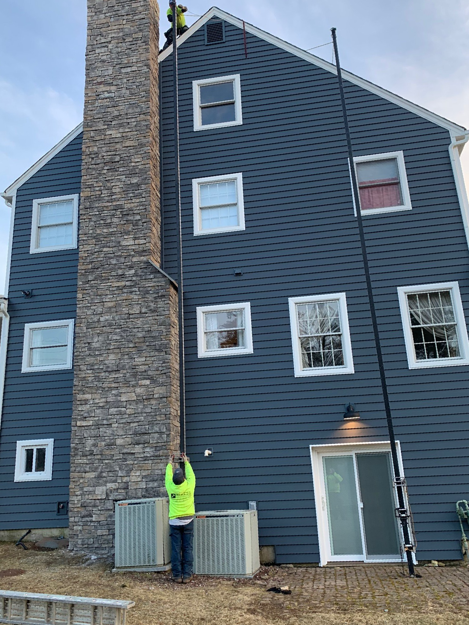Blue building with stone chimney; person in neon vest standing by the entrance.