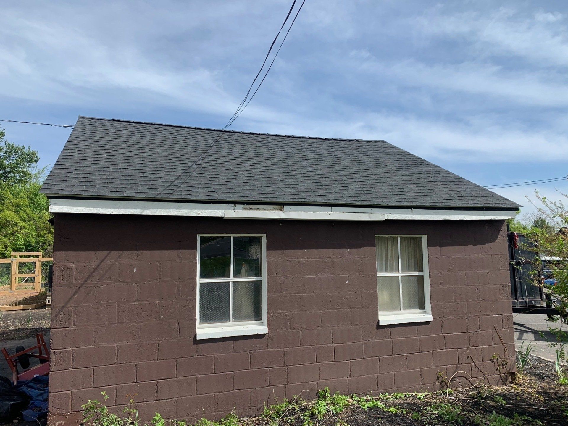 Small brown cinderblock shed with a dark shingled roof and two windows under a blue sky.