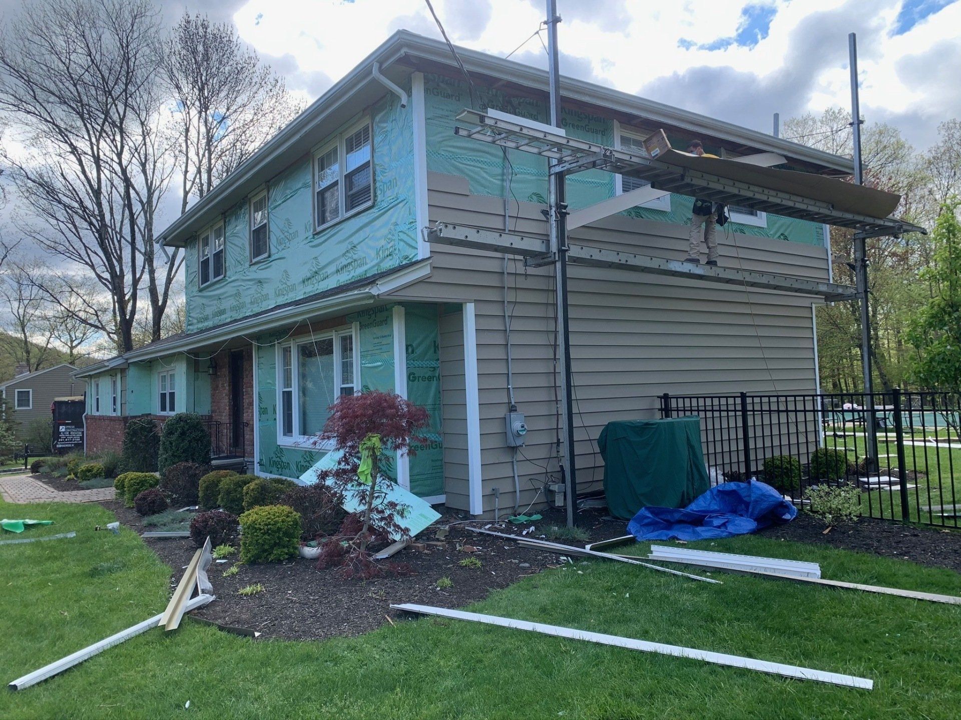 Two-story turquoise house with damage, debris in the yard, and a blue tarp near the side.