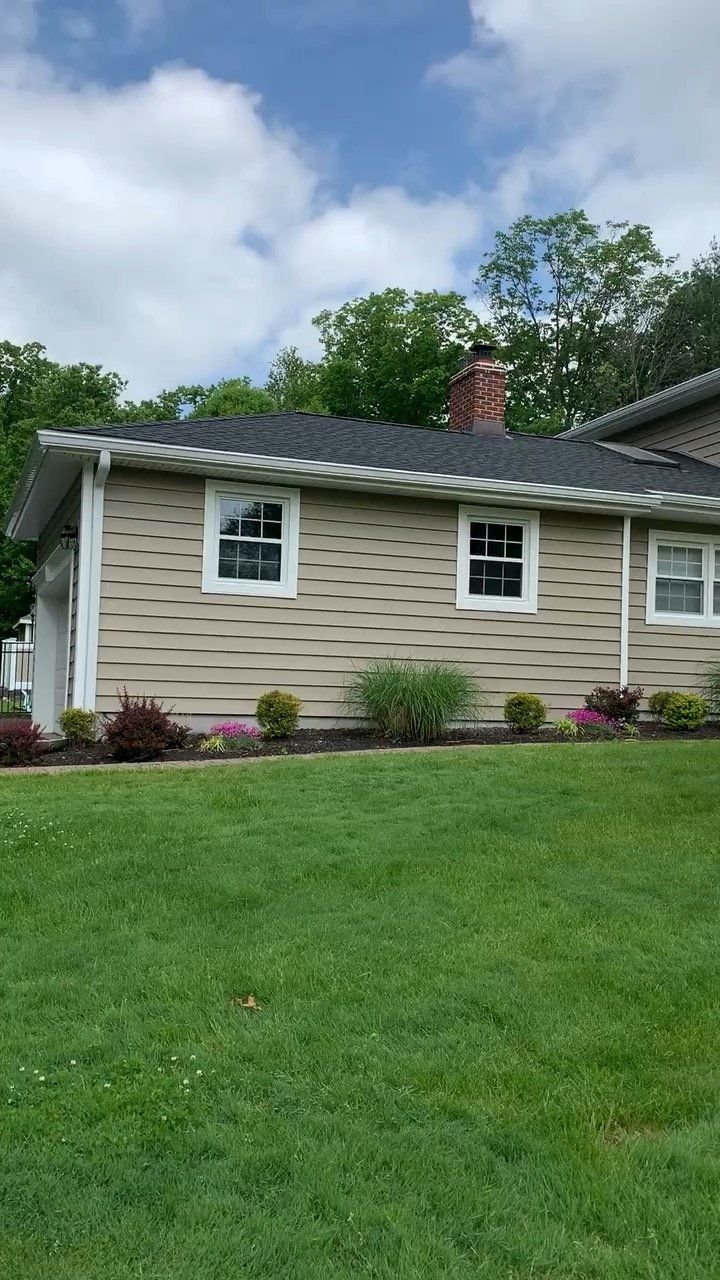 Suburban house with beige siding, white windows, and green lawn under trees