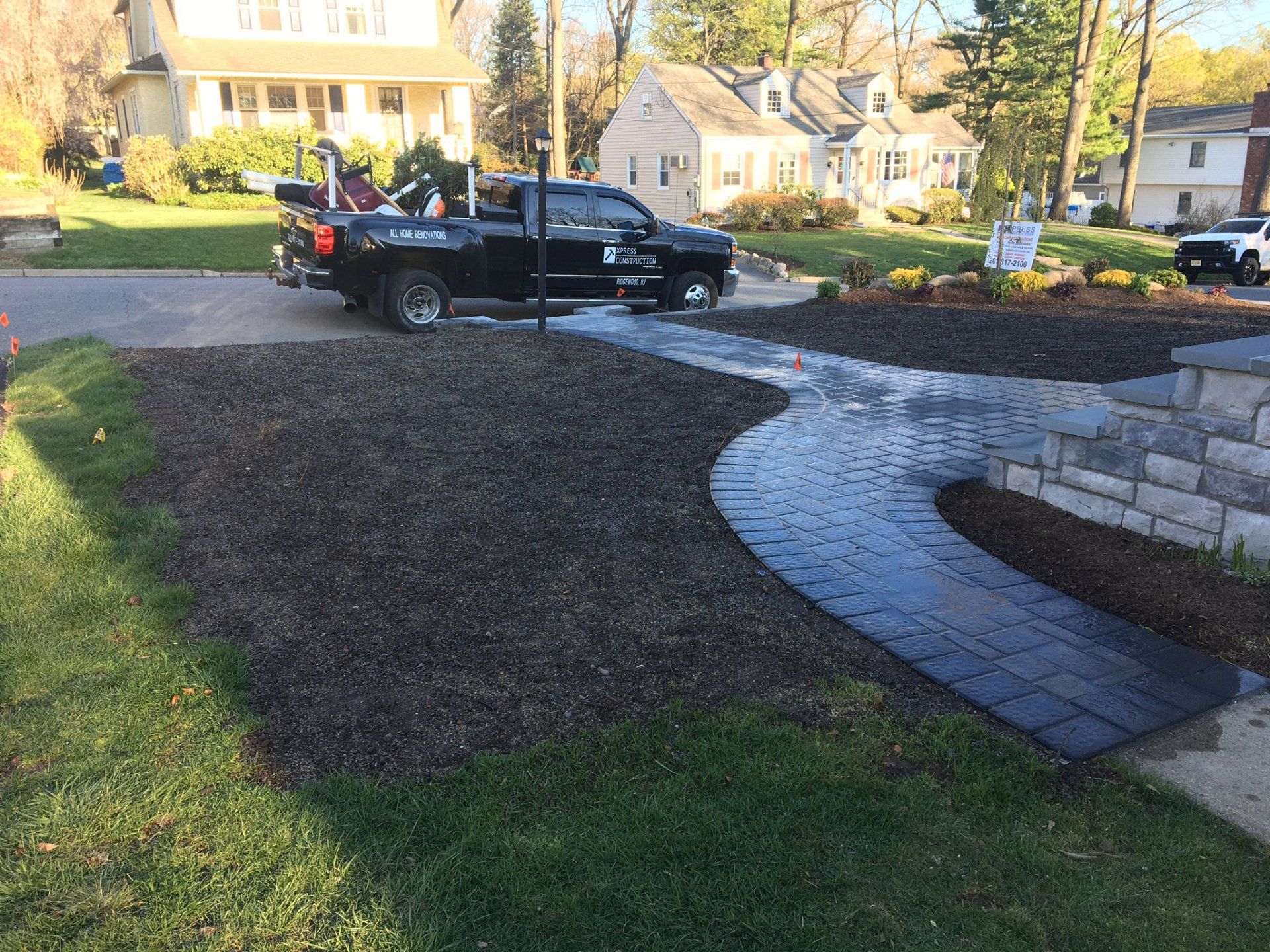 Black pickup truck on a driveway beside a curved stone walkway and landscaped yard.