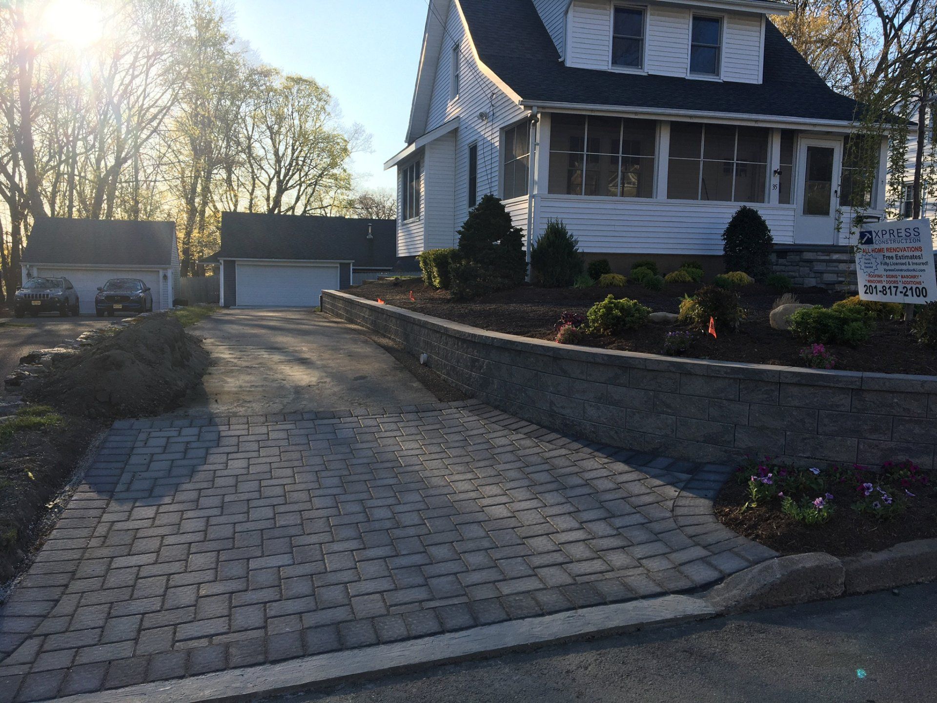 Brick driveway leading to a two-story house with garage at sunset