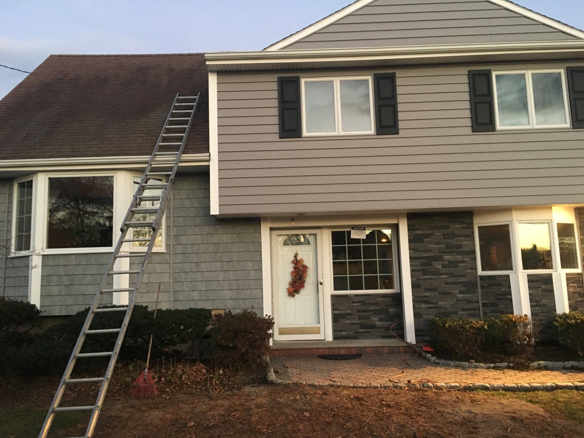 Two-story house with a ladder leaning against the roof and front facade, exterior siding in gray and brown.