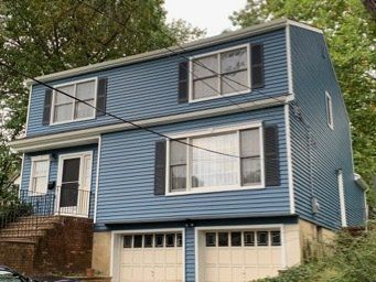Blue two-story house with white trim and a double garage on a sloped lot