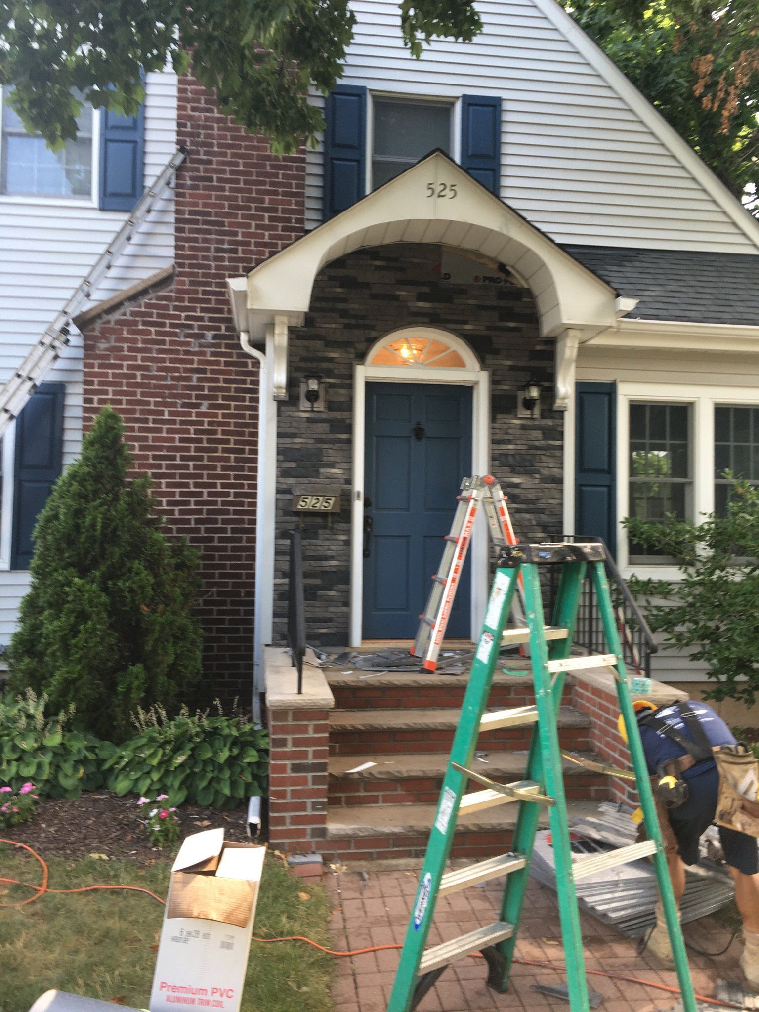 Two workers repairing the front entrance of a house, with ladders, tools, and a partially restored porch.
