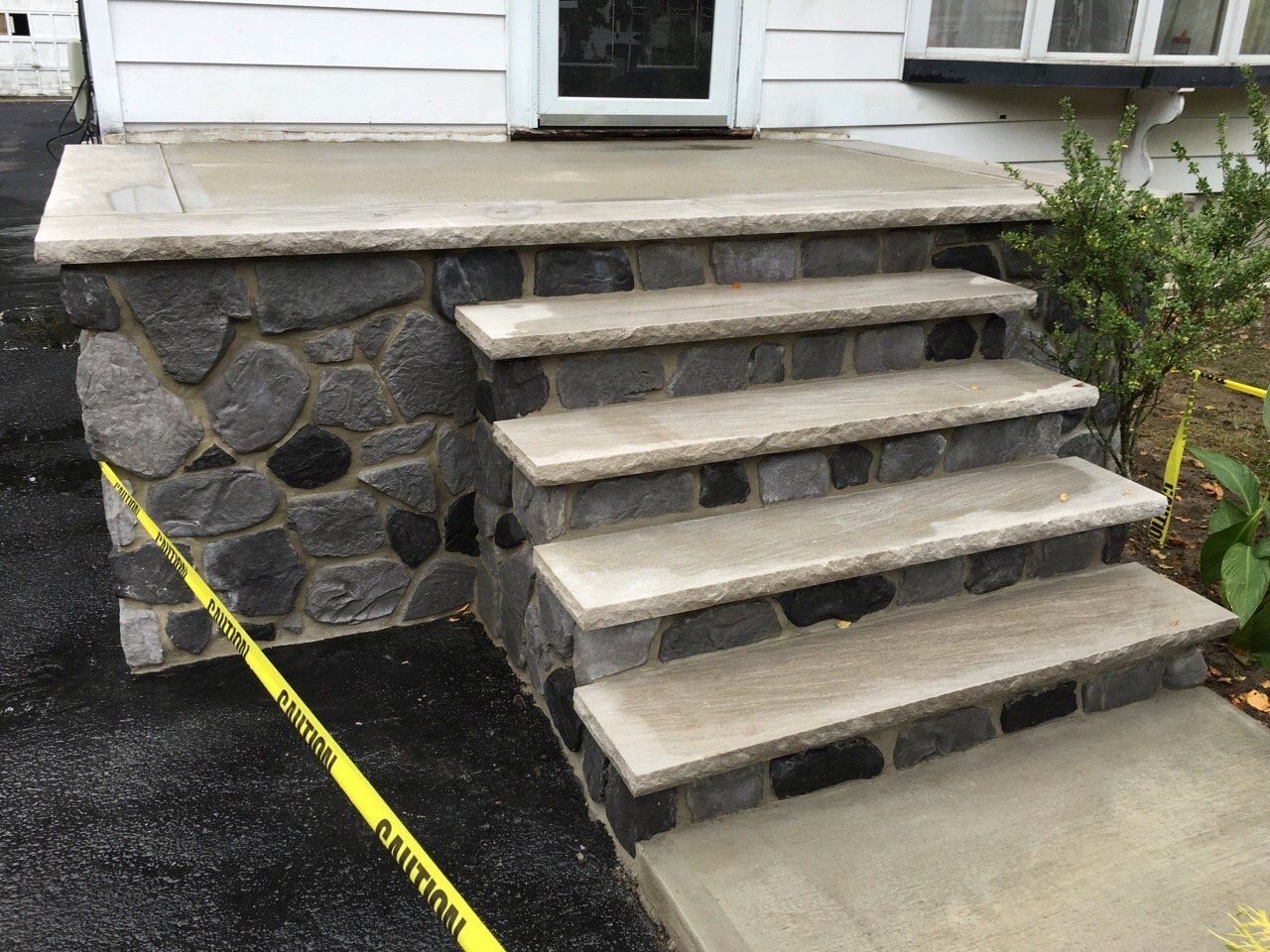 Concrete steps leading to a porch beside a stone retaining wall and yellow caution tape