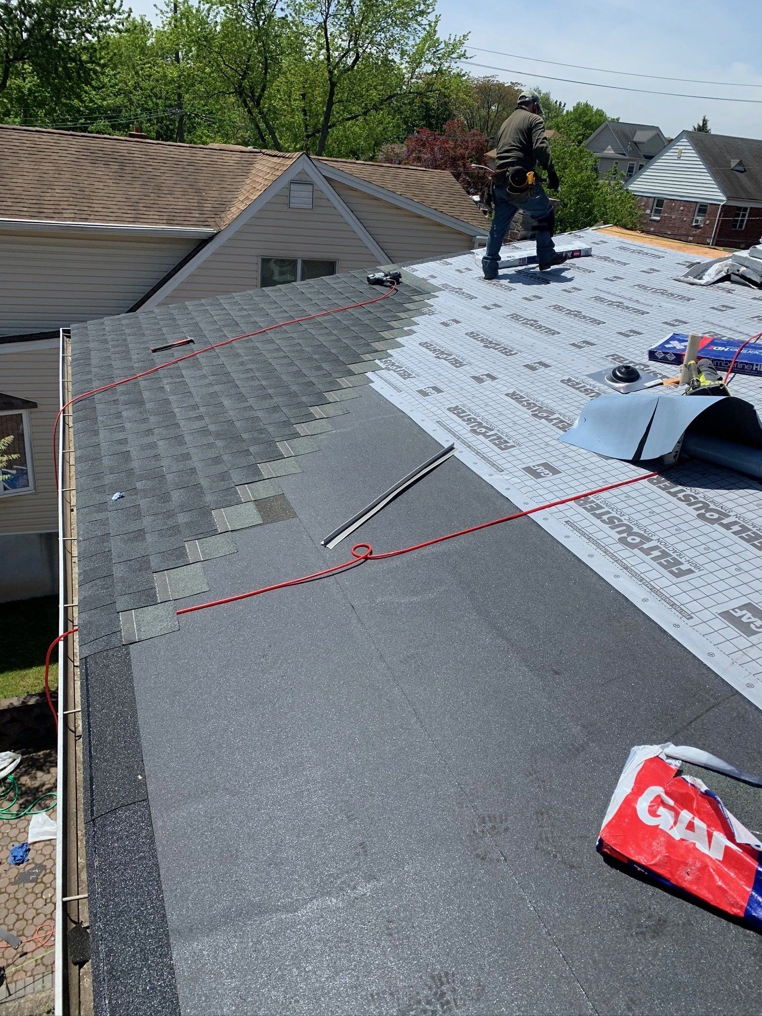 Roofers installing new shingles on a sloped gray roof, with roofing materials and tools visible.