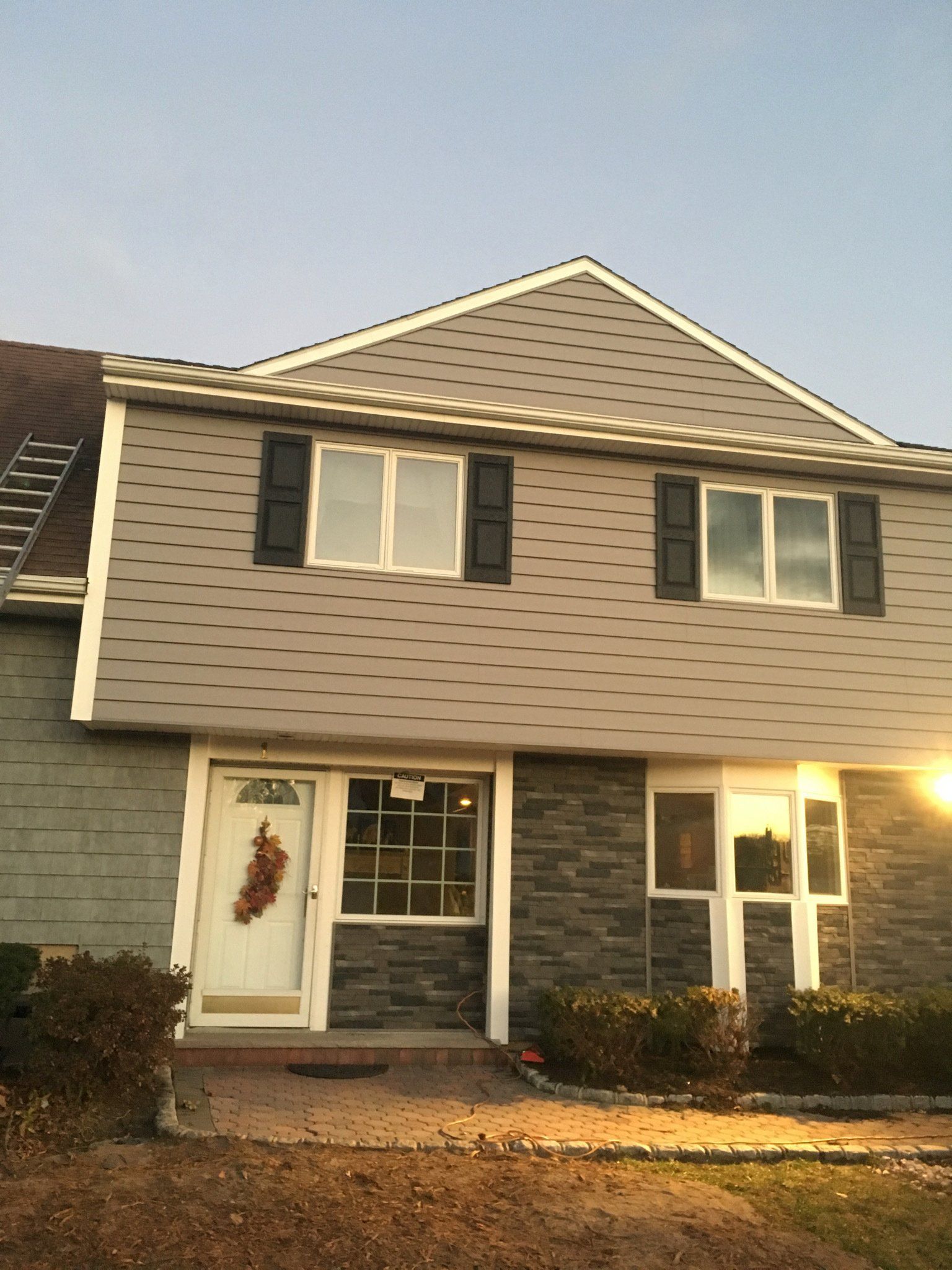 Two-story gray house with black shutters and a white front porch at sunset
