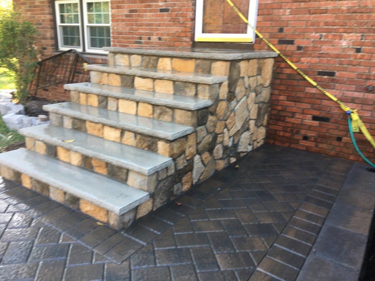 Stone steps beside a brick house with a paver patio and yellow strap railing nearby