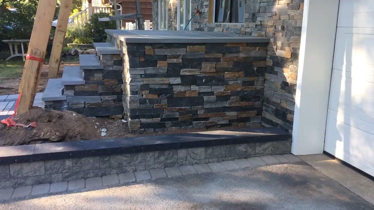 Front steps and stone retaining wall beside a driveway, with a white garage door.