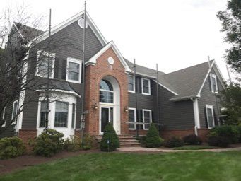 Brick house with dark siding, white trim, arched entry, and a manicured front lawn.