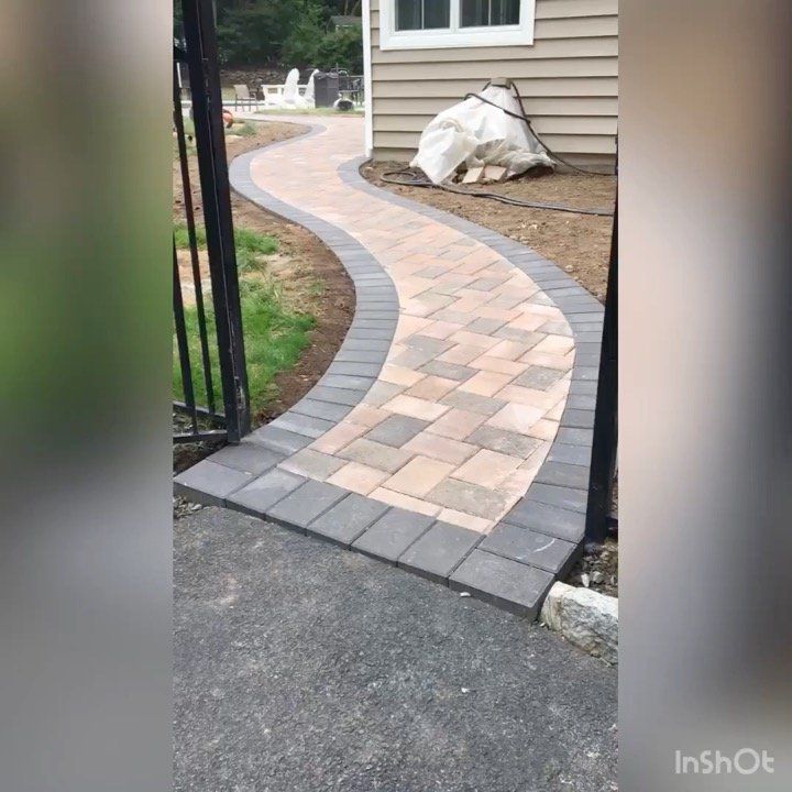 Curved brick walkway with gray border leading to a house entrance beside a beige siding wall.