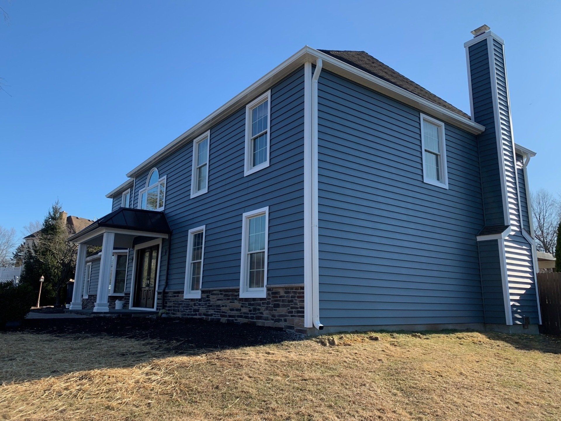 Gray two-story house with blue siding, white trim, and a covered front porch on a sunny day