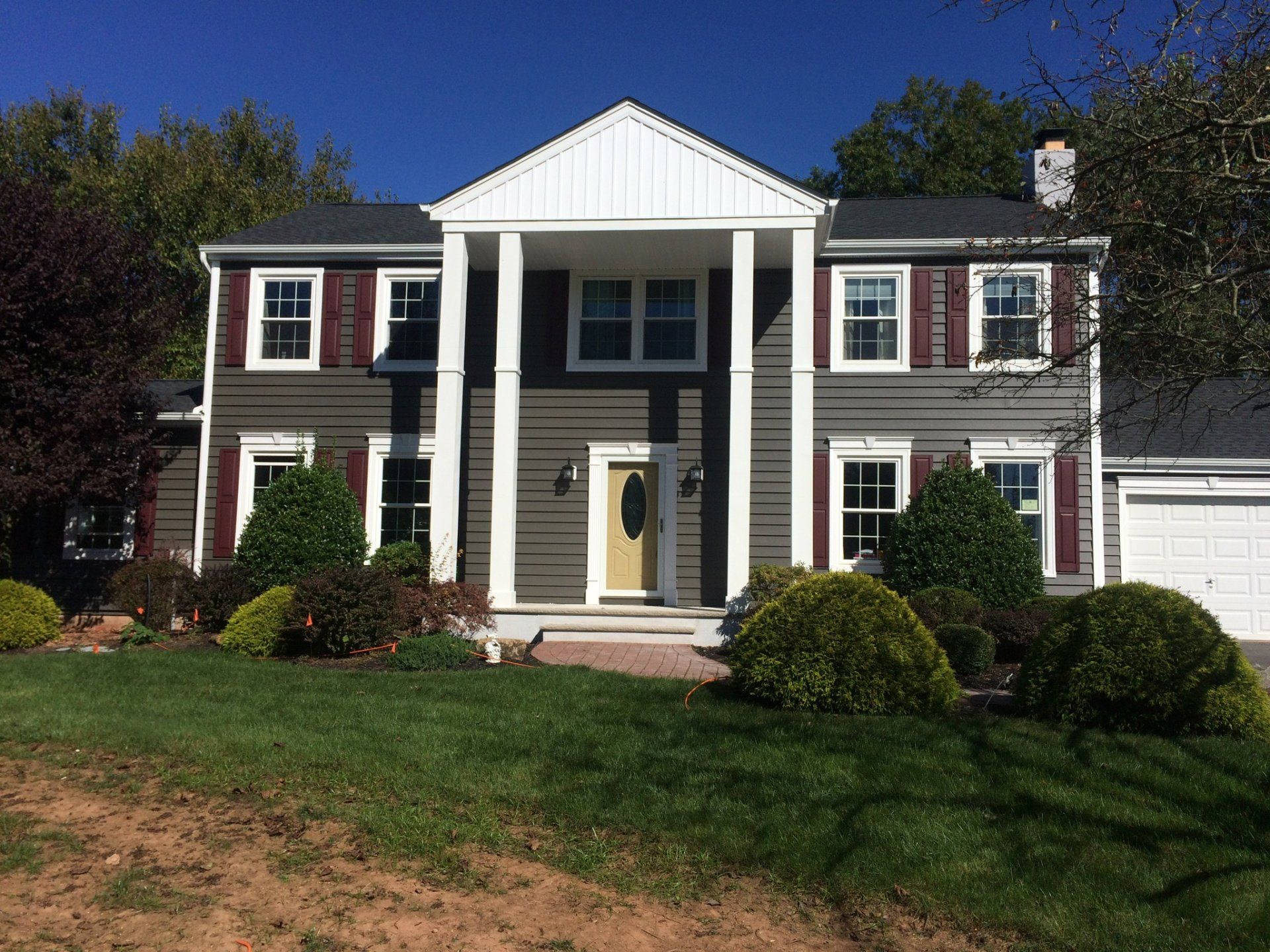 Two-story Colonial house with white columns, red shutters, and a green lawn in front