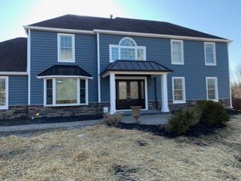 Two-story blue house with white trim, front porch, and winter-brown lawn