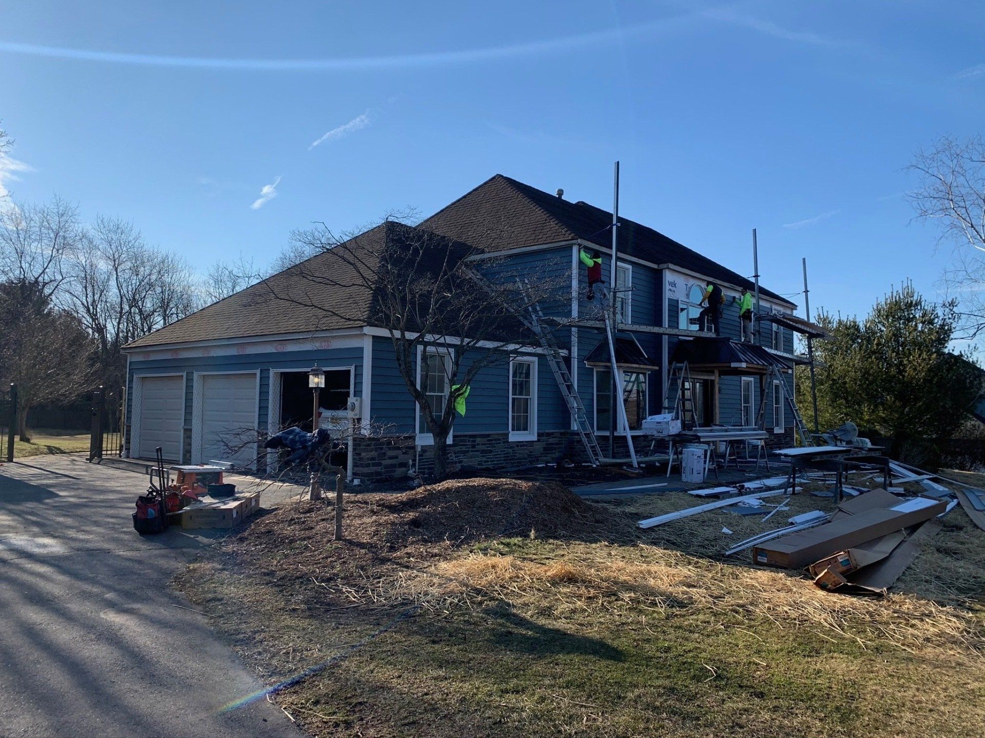 Partially renovated gray house with scaffolding and construction debris in a sunny yard