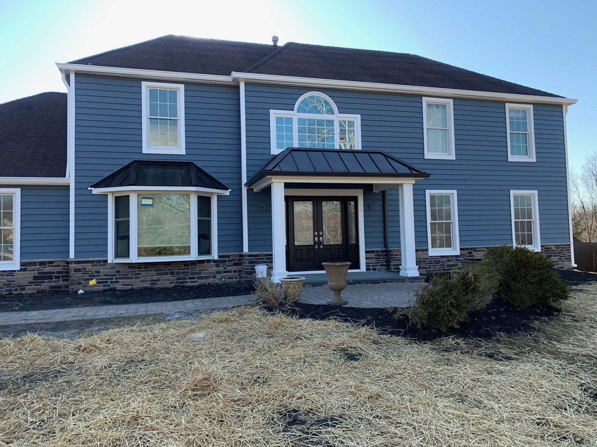 Two-story blue house with a dark roof, white trim, and a front porch over a dry front yard.