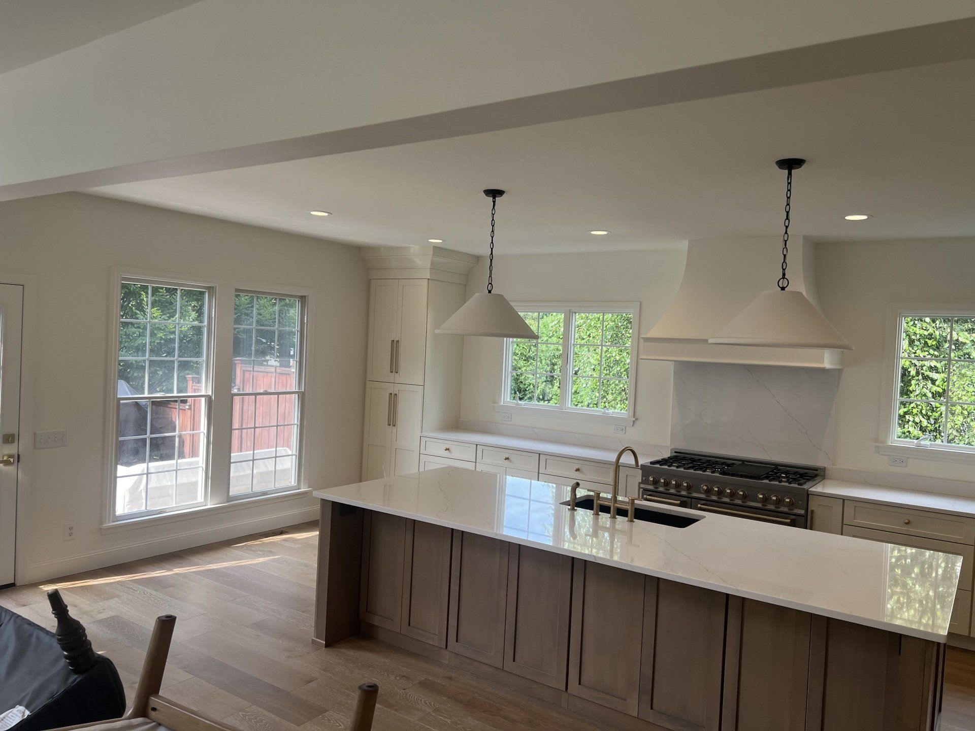 Bright modern kitchen with island, white countertops, pendant lights, and large windows overlooking a yard