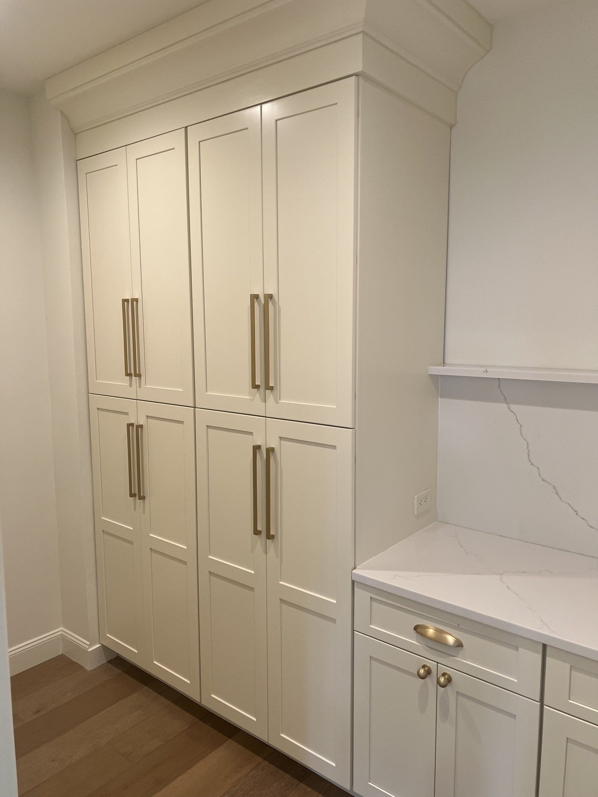 Built-in white cabinets and drawers with gold handles in a bright kitchen hallway