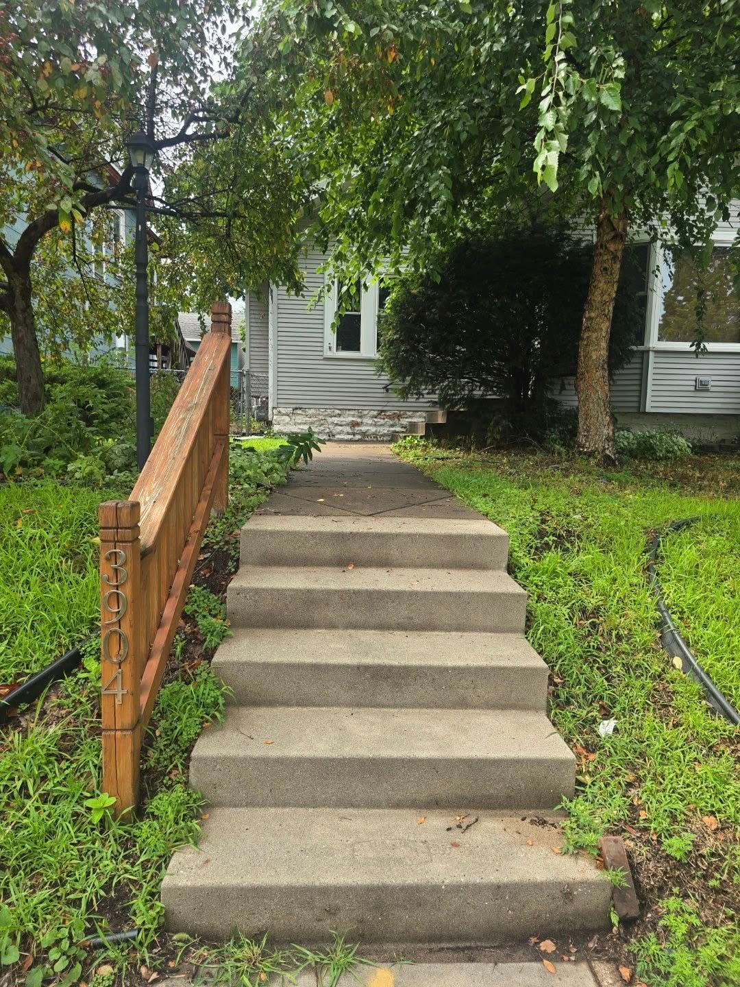Concrete steps leading to the front of a gray house, with a wooden handrail on the left featuring the house number 2304.