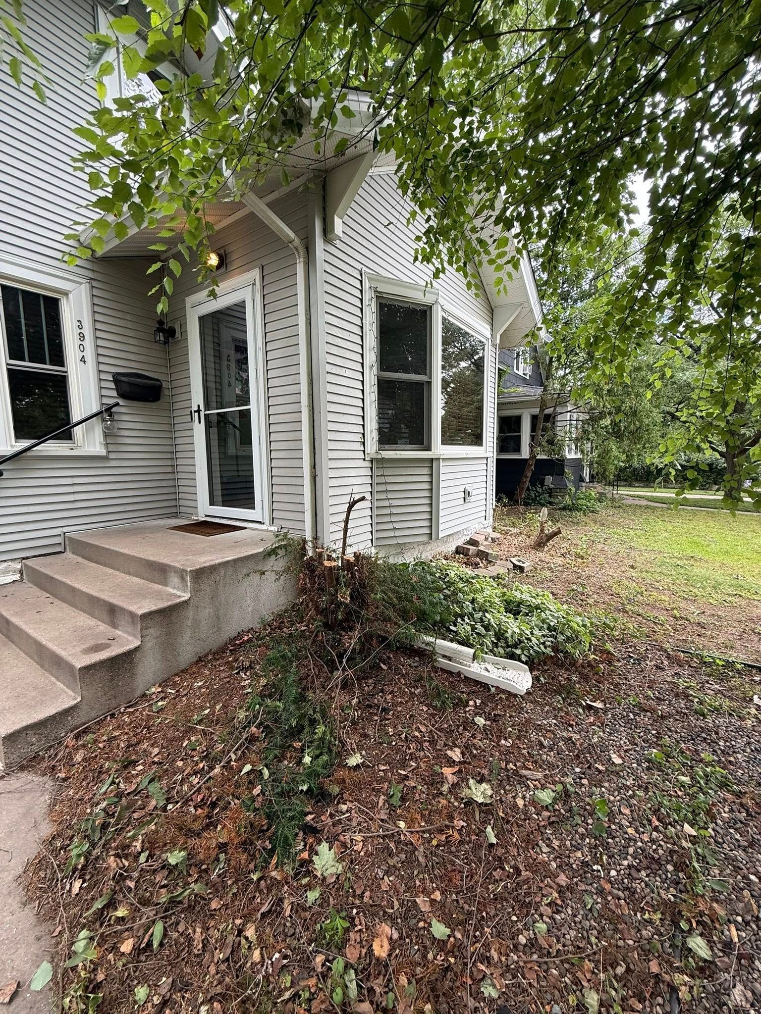 A side view of a white, shingled house with a small staircase leading to an entrance, surrounded by fallen brown leaves.