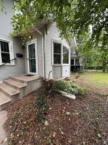 A side view of a white, shingled house with a small staircase leading to an entrance, surrounded by fallen brown leaves.