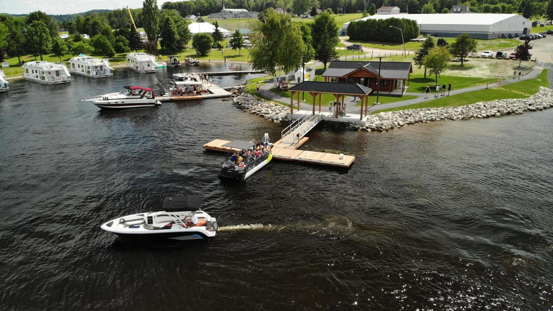 Boats at a dock on a lake, near a building and houses.