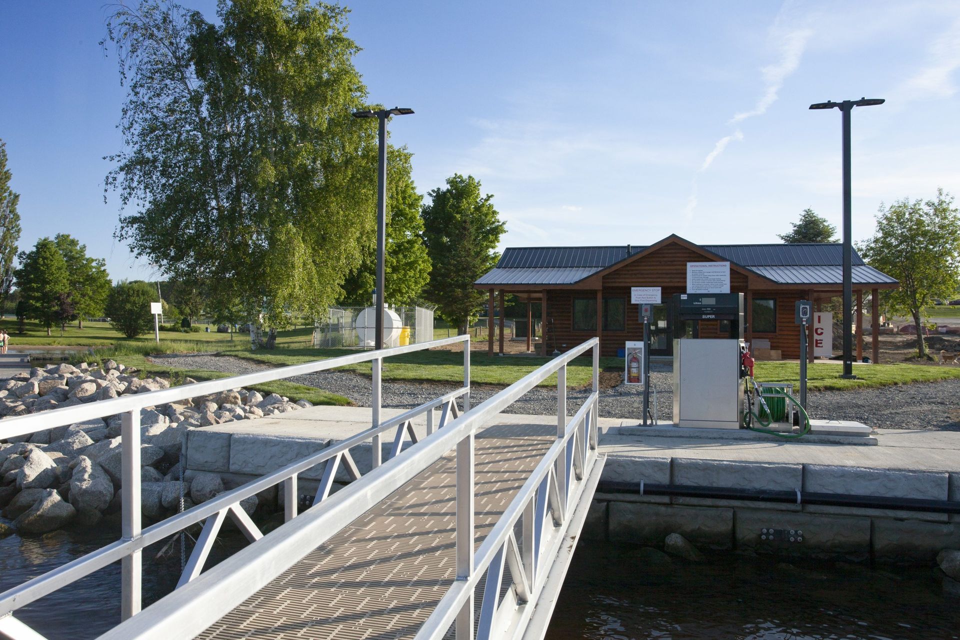 Wooden pier leading to a small wooden building on a lake. Trees and blue sky are in the background.